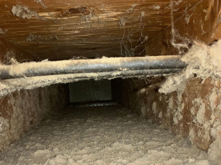 Inside residential ductwork before cleaning. Electrical wire going through the ductwork. Obvious layer of dust and debris accumulated in the ductwork and on the electrical wires.