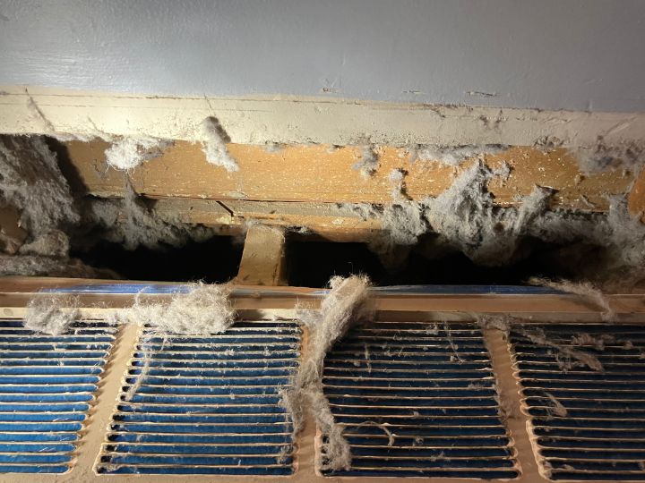 Air intake register before being cleaned. Large layer of dust and debris accumulated around the vent.