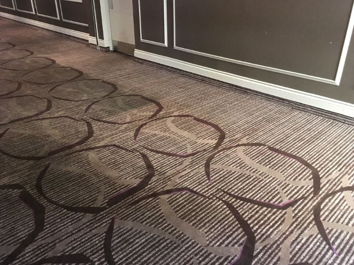 Patterned Commercial carpet while being cleaned by the Klean & Brite team. One portion of the carpet is clean and bright, the other is still covered with embedded dirt and grime.