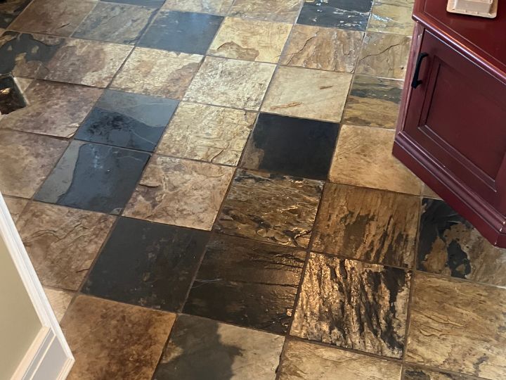 Patterned and textured ceramic tile floor before being cleaned. Dirt covered, grout appears dark brown in colour.