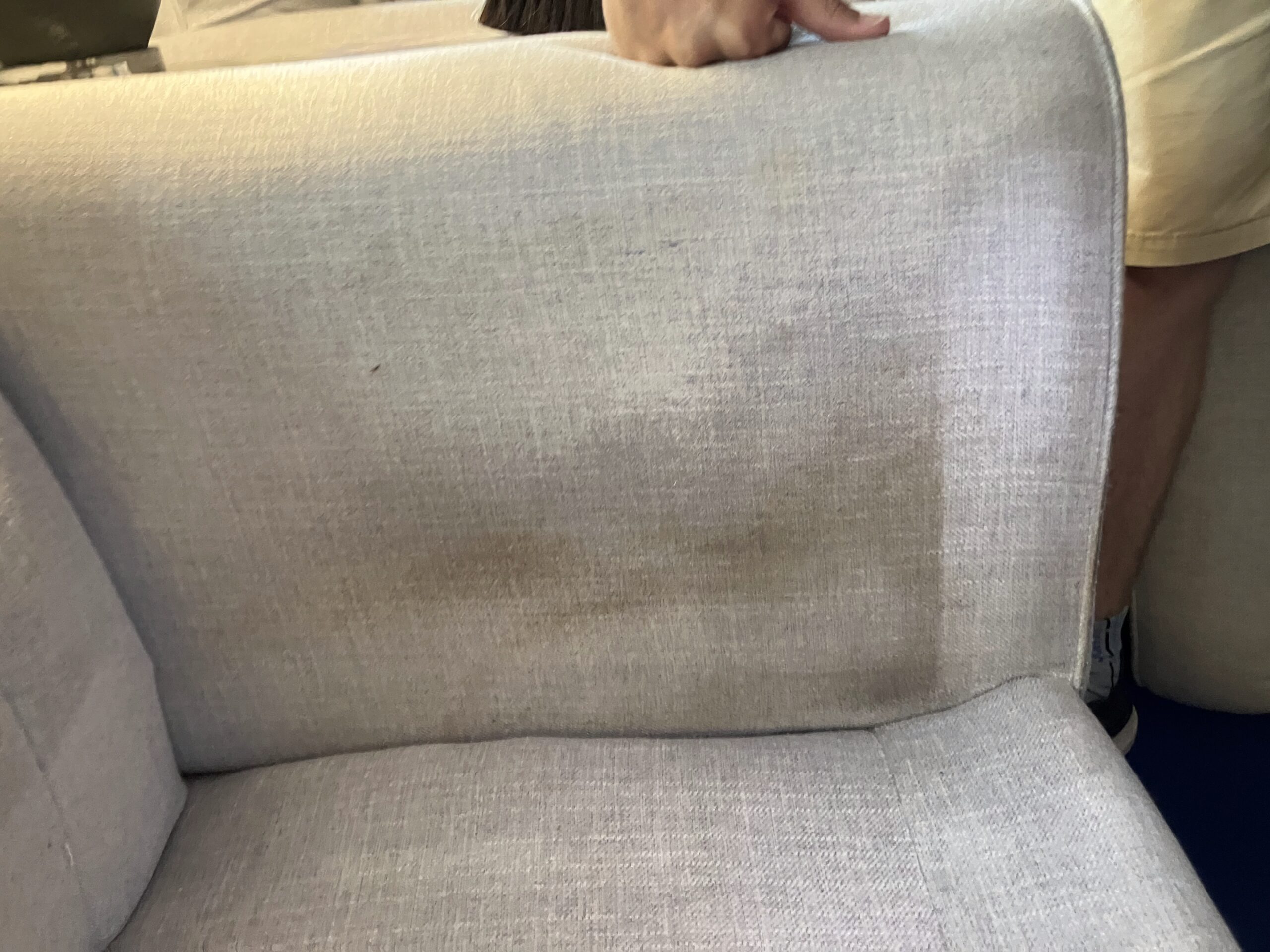 Close-up of the side of a couch where on spot has been steam cleaned. The cleaned spot is a new-looking bright light grey whereas the rest is browned and dirt-covered.