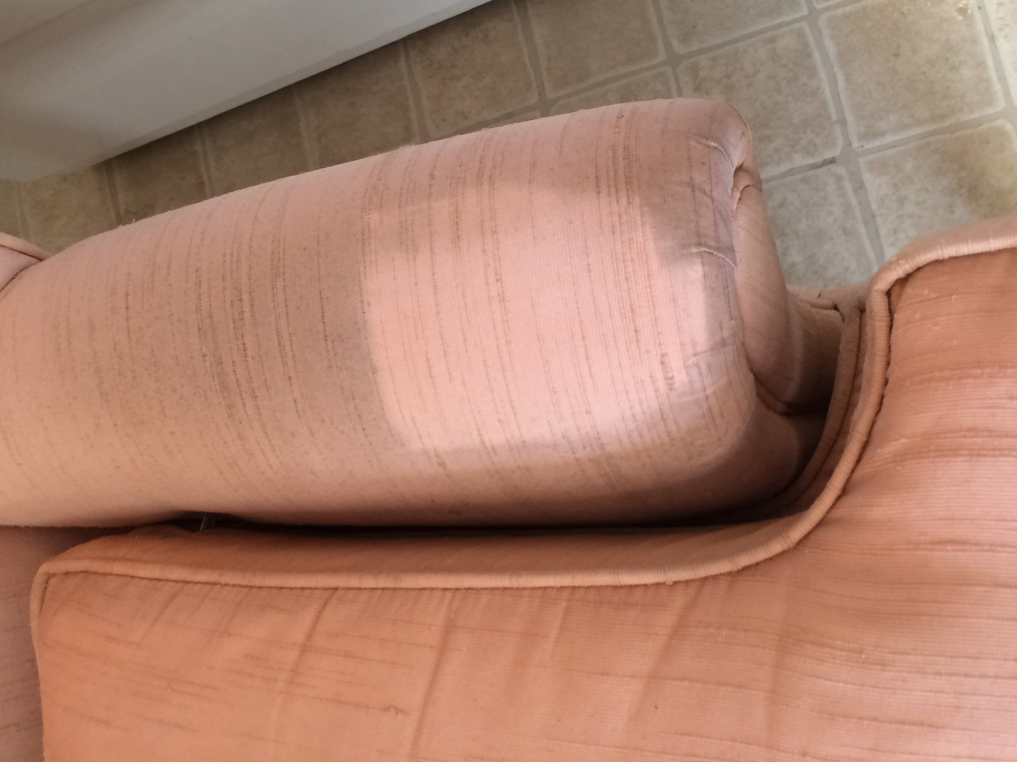 Close-up of the arm of an upholstered chair with one spot cleaned. The cleaned spot is bright and new looking. The rest of the chair is browned and dirt covered.